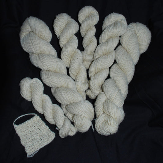 White skeins of yarn and a small knitted item on a dark background