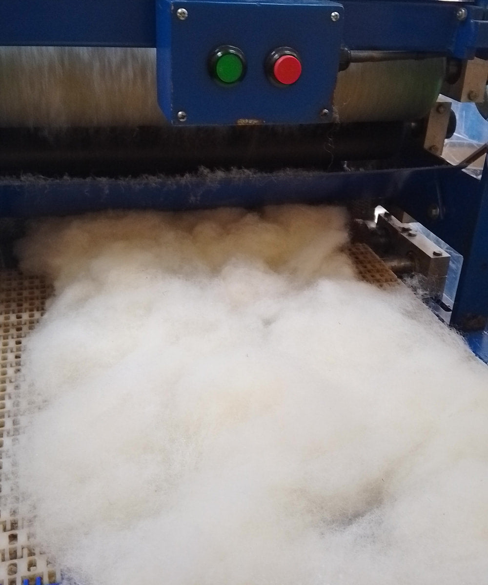 Close-up of a machine processing white fibres with blue machinery and control buttons.